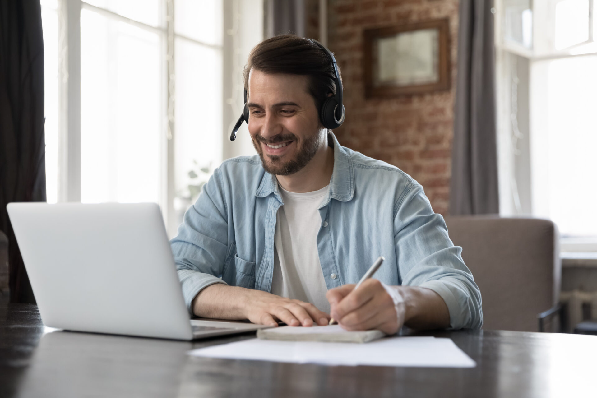 Man wear headset studying online seated at desk with laptop