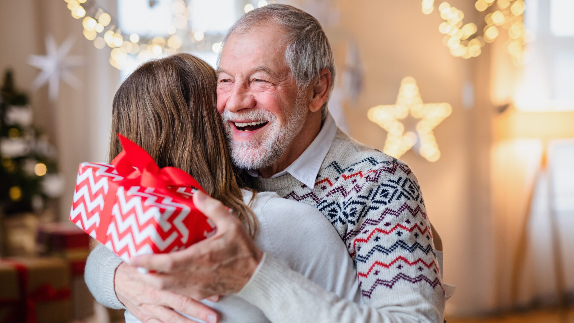 Young woman giving present to happy grandfather indoors at home at Christmas.